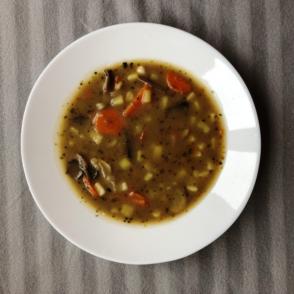 Bramborová polévka s houbami a zeleninou v bílém talíři na šedém pozadí, poctivá bramboračka s houbami